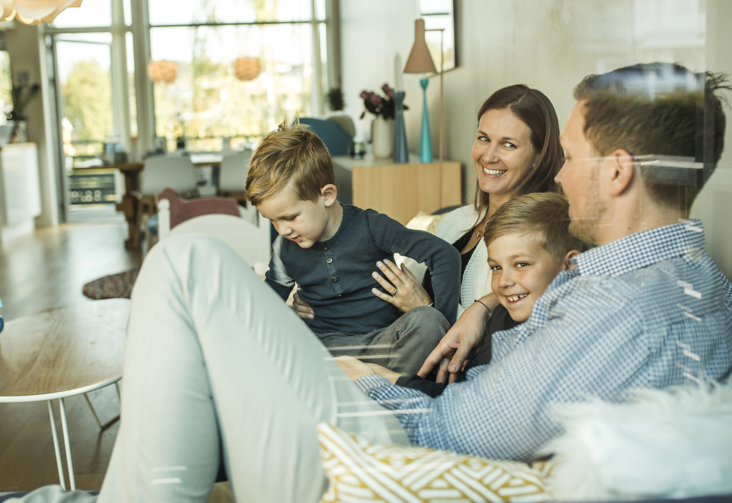 Familie med to børn og to voksne sidder i sofa, de voksne smiler til hinanden, fotografi