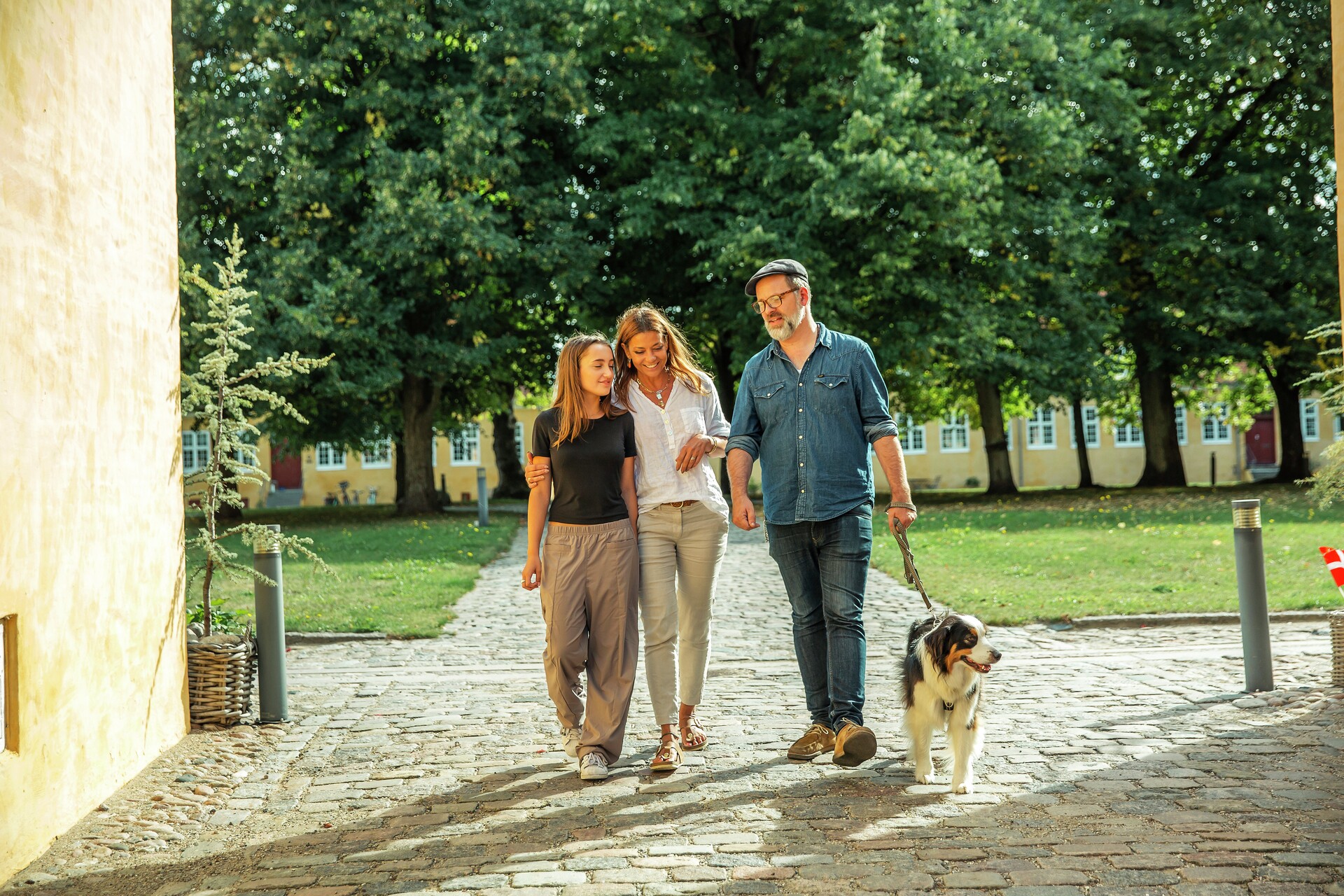 Familie med far, mor og datter går i tur i park med hund, fotografi