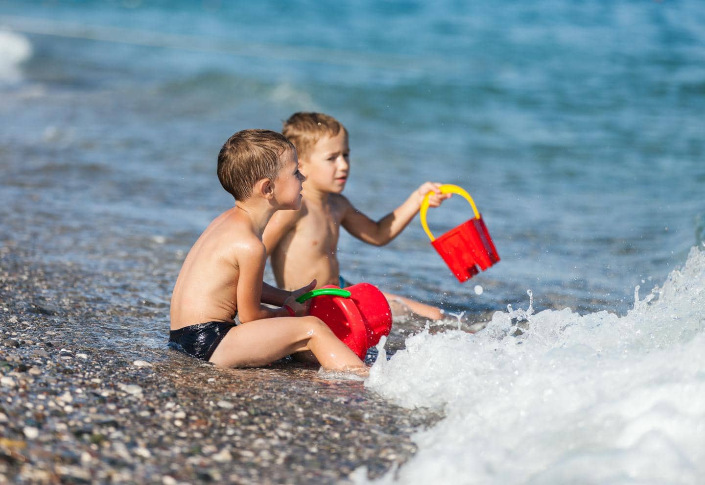 Børn i strandkanten, der leger med spande og vand